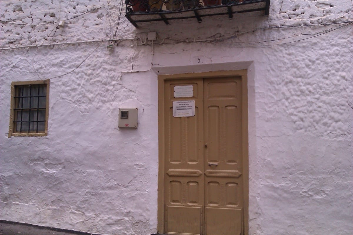 Fachada encalada de la casa de las caras, con la puerta de madera del número 5 y dos carteles pegados