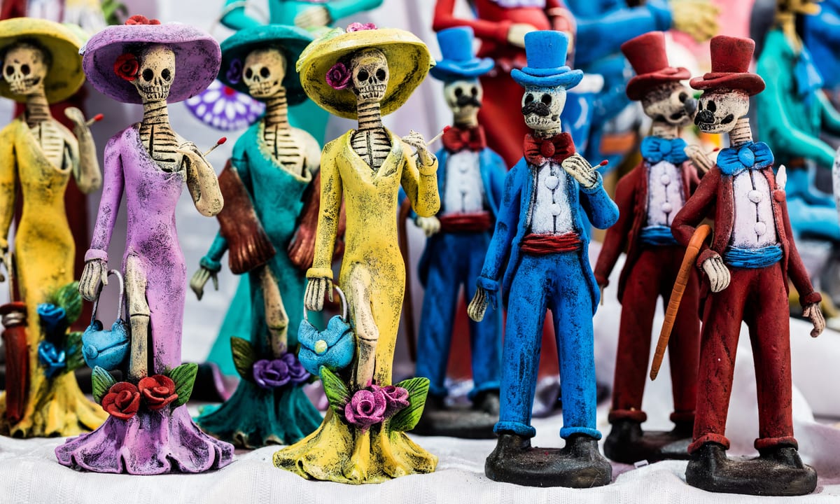 Figuras de catrinas con vestido largo, sombrero y bolso junto a catrines con chistera y pajarita, todas de colores