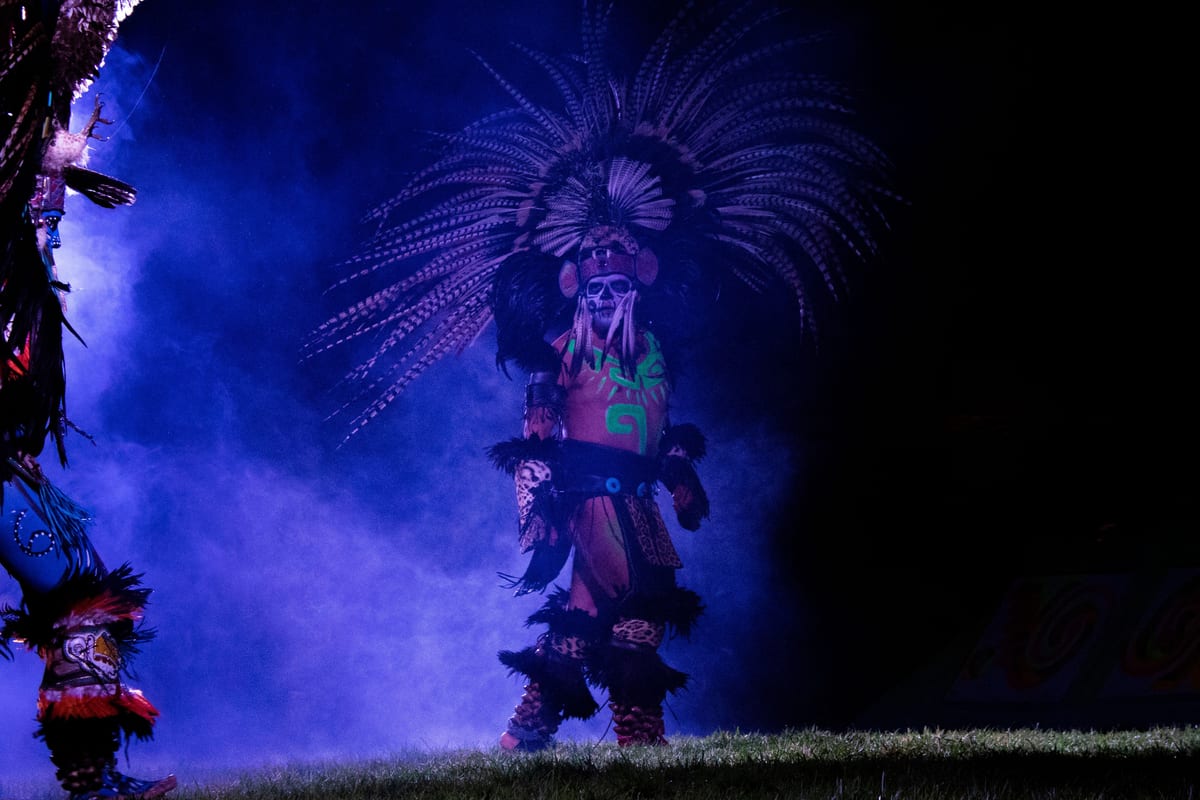 Un danzante con penacho de plumas y máscara de calavera entre humo violeta, de noche, en la función de Xochimilco