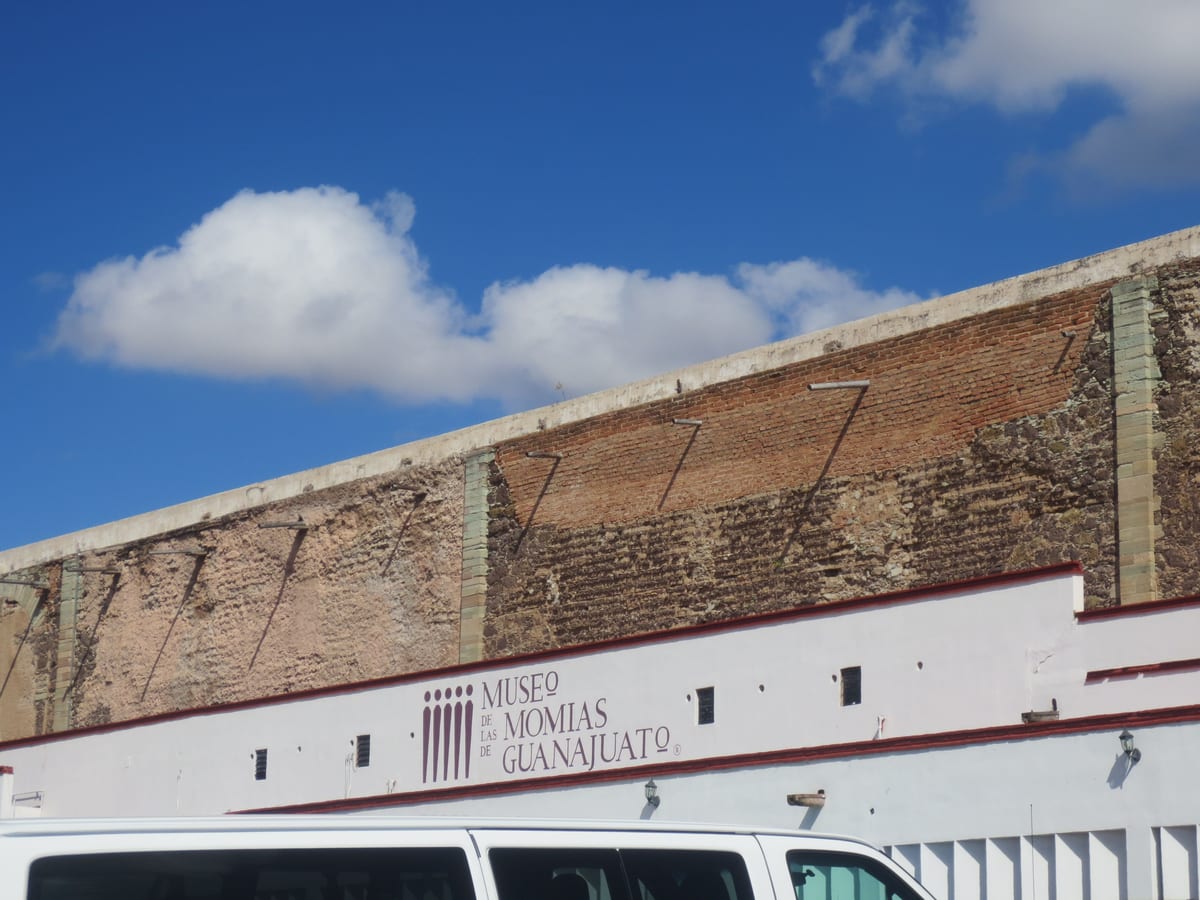 Muro de piedra y ladrillo del Museo de las Momias de Guanajuato con su letrero, bajo un cielo azul