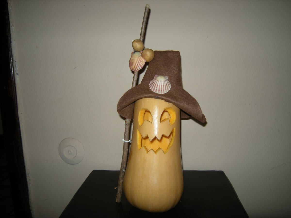 Calabaza alargada con cara tallada, sombrero de fieltro marrón, bastón y conchas de vieira de peregrino