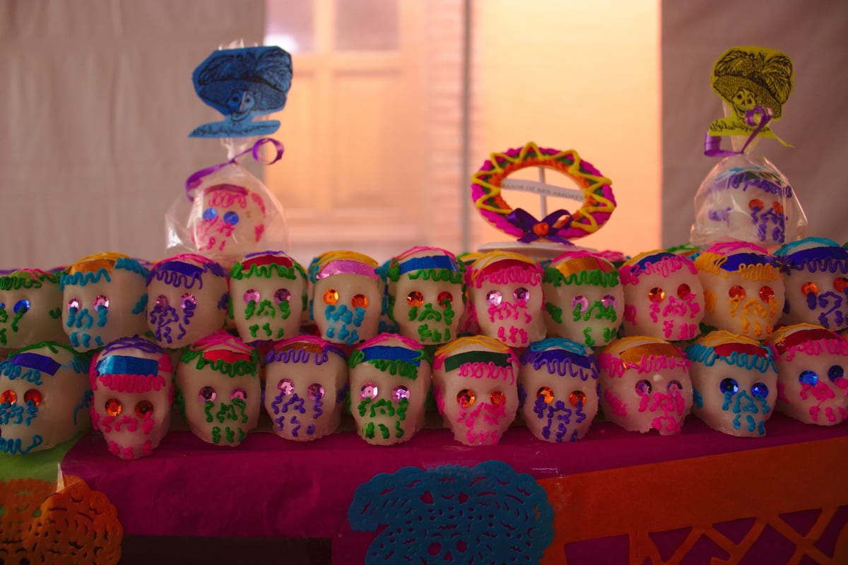Filas de calaveras de azúcar blancas con ojos de papel brillante y adornos de colores en un puesto