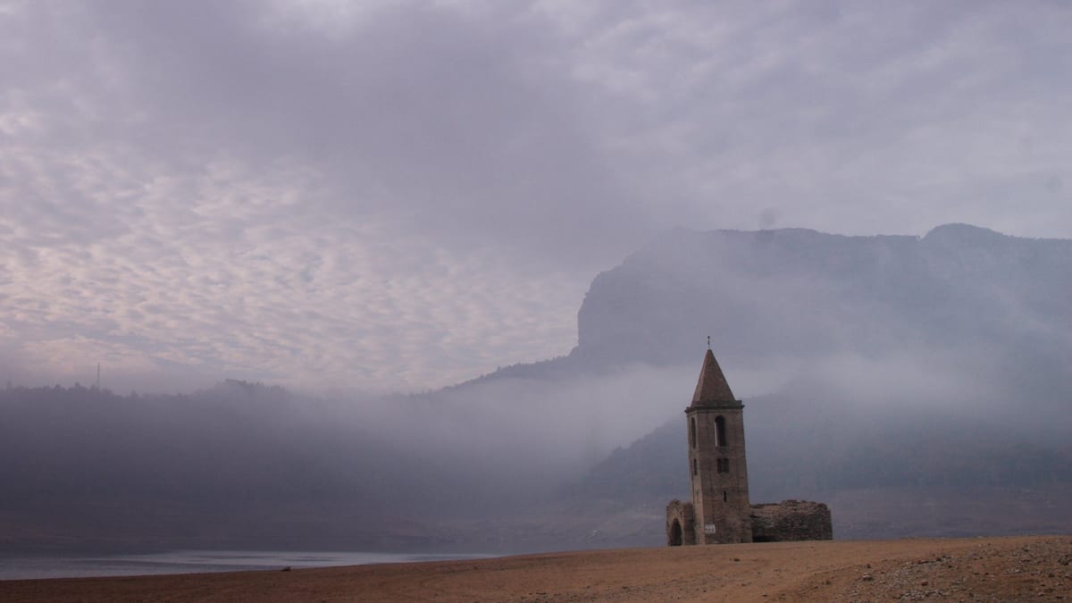 La iglesia de Sant Romà de Sau en el fondo seco del pantano, entre la niebla, con un risco detrás